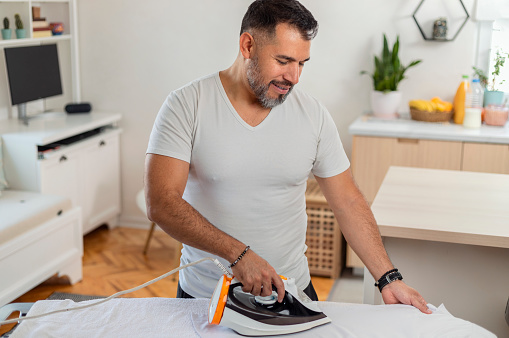 Closeup front view of a handsome mature man ironing his white shirt.