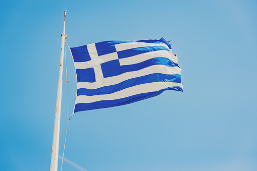 Low angle close-up view of Greek flag waving against clear blue sky during sunny day