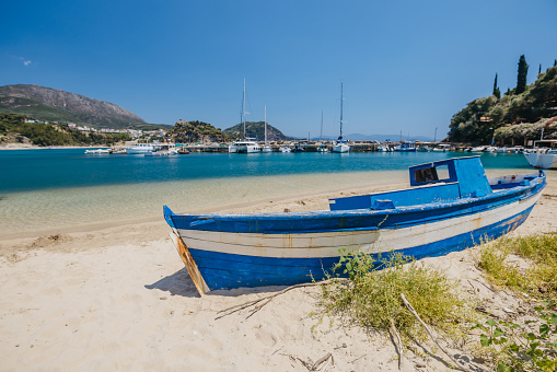 Old blue boat moored at sandy beach by harbor against clear sky during sunny day