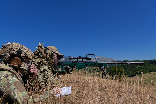 A sniper team squad of soldiers is going undercover. Assisted by an assistant to observe the area to be targeted with modern warfare tactical virtual reality goggles aerial drone military technology.