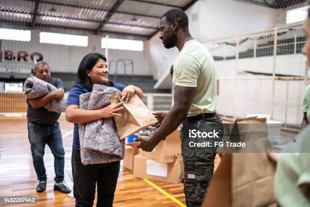 Mature Woman Receiving Food And Blanket From A Soldier At A Community Center Stock Photo - Download Image Now