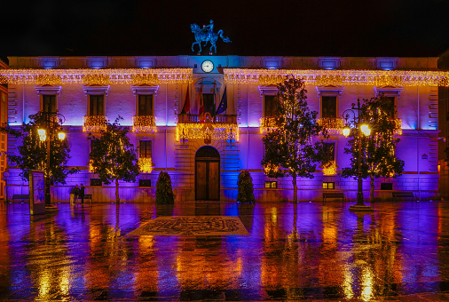 Granada, Spain, 1 December 2019. Town Hall square and façade decorated with Christmas lights on a rainy night.
