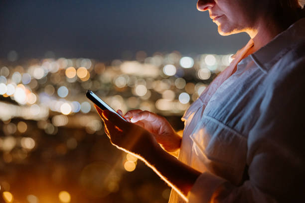 istock Tourist using smart phone while standing against illuminated cityscape 1432208318