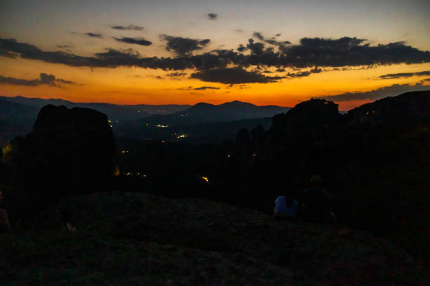 Couple sitting together on mountain against orange sky during sunset
