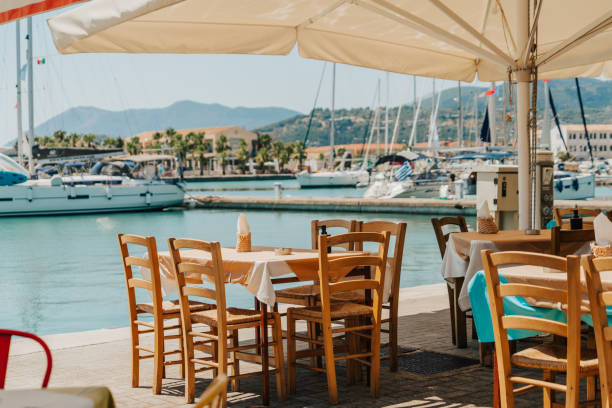 istock Tables and chairs arranged at coastal restaurant by harbor in city 1432209868