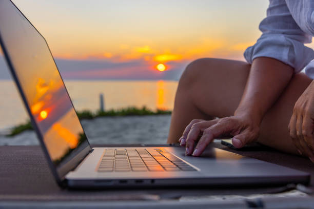 istock Midsection of woman using laptop while sitting on chair at beach during sunset 1432210124