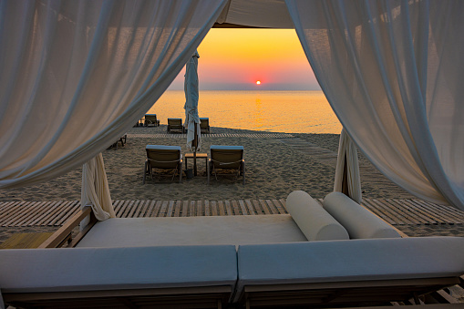Luxurious lounge chairs at sandy beach against orange sky during sunset