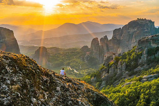 Tourist relaxing on rock while exploring Meteora Monastery against orange sky during sunset