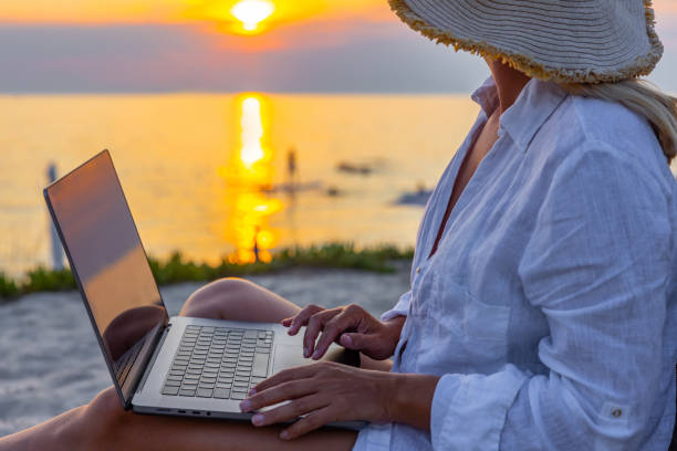 istock Woman using laptop while relaxing on lounge chair at beach during sunset 1432211811