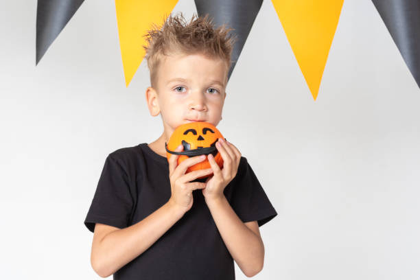 istock Halloween kids boy with pumpkin buckets eating candy on a white studio background with a garland 1432212407