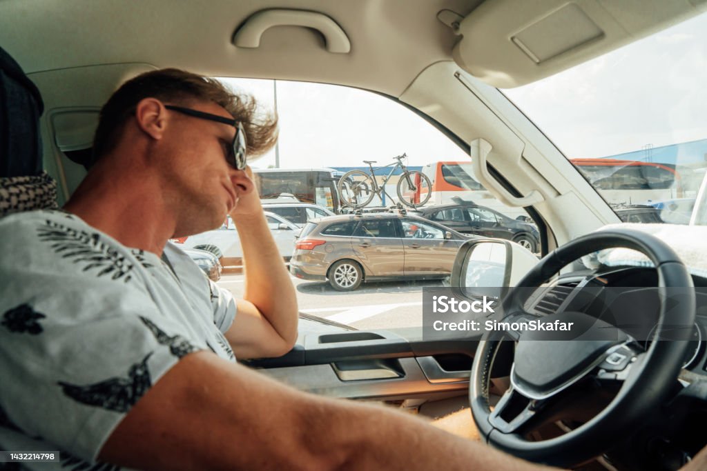 Worried and tired man sitting inside car in heavy traffic Bored and tired man wearing sunglasses while sitting inside car in traffic jam during rush hour Driving Stock Photo