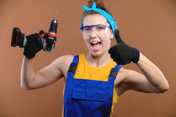 istock Attractive smiling young female builder with tool in hand in uniform showing thumb up. studio shot 1432216879