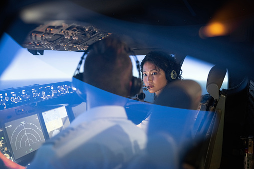 Female trainee pilot listening to her instructor's advice during a training session in flight simulator. Woman learning to flight an airplane with instructor inside a flight simulator.