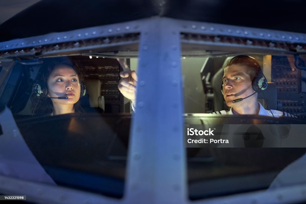 Pilot teaching a female student to fly a plain inside a flight simulator Flight instructor is describing different dials and switches to a trainee pilot in the cockpit of a simulator. Pilot teaching a female student to fly a plain inside a flight simulator. Pilot Stock Photo
