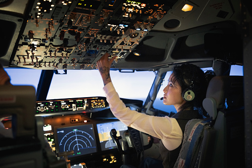 Rear view of a female pilot adjusting switches on the control panel while sitting inside cockpit. Woman operating the switches while flying an airplane.