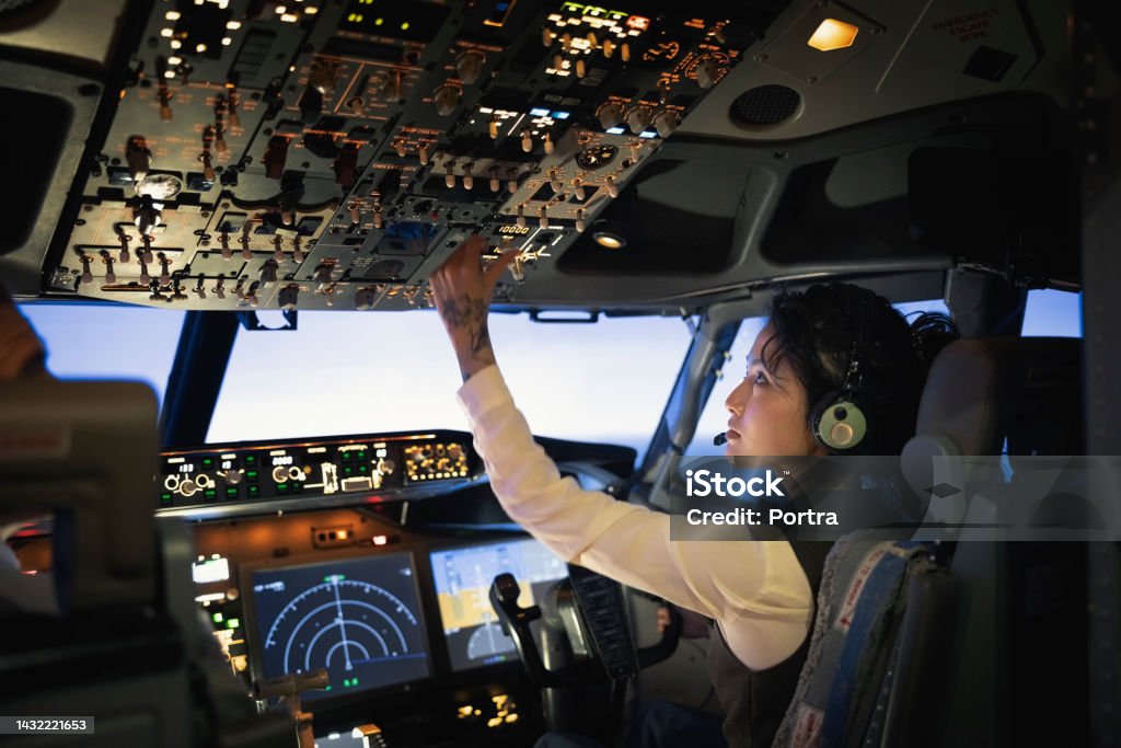 Rear view of a woman pilot adjusting switches while flying airplane Rear view of a female pilot adjusting switches on the control panel while sitting inside cockpit. Woman operating the switches while flying an airplane. Pilot Stock Photo