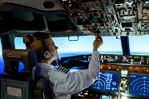 Rear view of a male pilot adjusting switches on the control panel while sitting inside cockpit. Man operating the switches while flying a modern airplane jet.