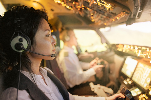 Side view of a female pilot with male co-pilot flying an airplane. Woman pilot with headset inside airplane cockpit.