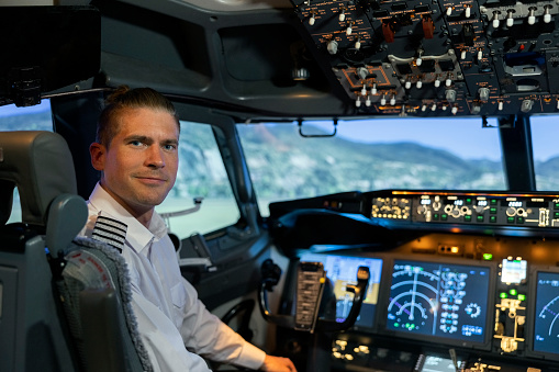 Portrait of a male flight instructor sitting in cockpit looking behind at the camera. Male pilot in uniform in flight simulator.