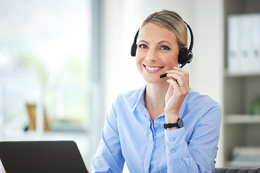 Contact us, customer service and telemarketing call center agent using her laptop and headset in the office. Portrait of a woman at our sales help desk job, smile and working to tell you about us