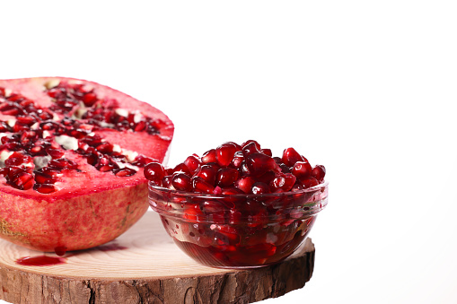 Ripe pomegranate fruit with sweet red seeds in a wooden spoon on a white background.