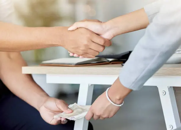 Photo of Business people agree to bribe and do handshake, giving money or cash payment below table. Employee or partnership make a deal for fraud, money laundering and corruption crime in a business meeting