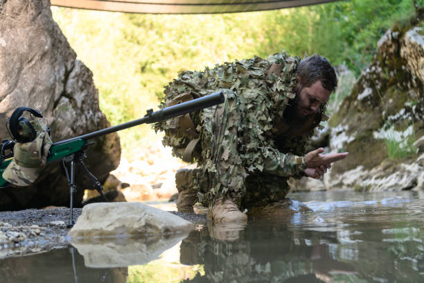 迷彩服を着た兵士が川から新鮮な水を飲む。側面に軍用スナイパーライフル。 - wet spy men suit ストックフォトと画像