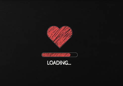 Loading is written below red heart shape on black chalkboard. Horizontal composition with copy space. Valentine's Day concept.