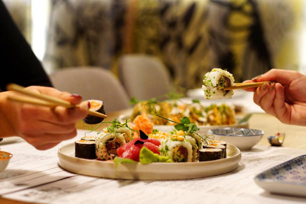 two women's hands holding sushi roll - sushischotel stockfoto's en -beelden