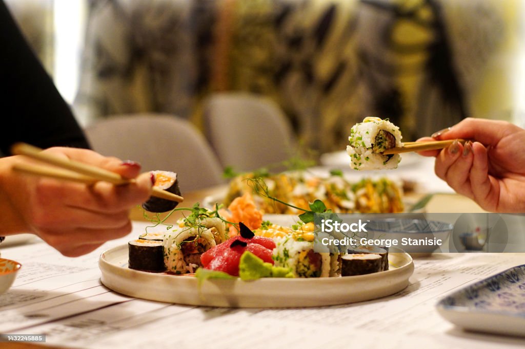 Two women's hands holding sushi roll Two women's hands holding sushi roll in restaurant. Sushi Stock Photo