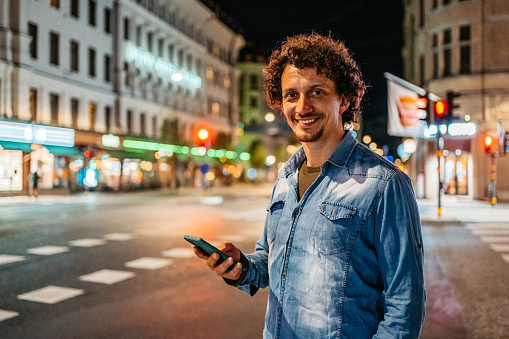 Portrait of a handsome young man standing in the city street and using his smart phone at night.