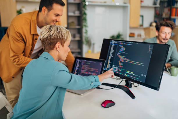 笑顔の男性プログラマーが、オフィスの机に座りながら、新しい女性同僚にコーディングテクニックを解説 - 放送プログラム ストックフォトと画像