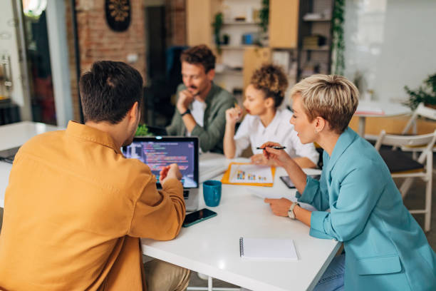 un programmatore maschio mostra a una collega una tecnica di codifica. i codici sono visibili sullo schermo del laptop - brainstorming team learning business foto e immagini stock