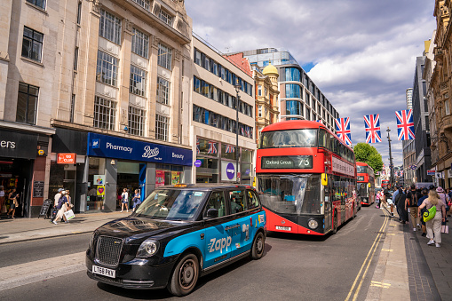 London Oxford Street with Red Bus and London taxi and people walking on street. Is a Westminster commercial street with more than 300 shops, crossing Oxford Circus. Starting in Marble arch to Hyde Park. With UK flags crossing the street and also LGTBIQ+ flags