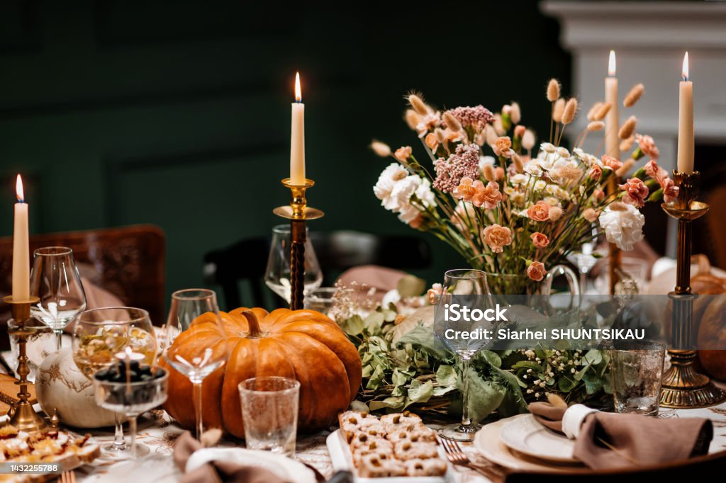 Decoration and serving of the festive table with autumn decor, candles and flowers and pumpkins and dishes. The Thanksgiving dinner table. A traditional Thanksgiving or Friendship Day party. Decoration and serving of the festive table with autumn decor, candles and flowers dishes and pumpkins. Candle Stock Photo