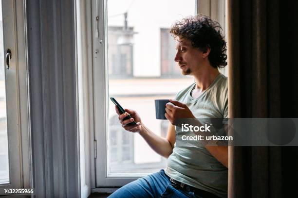 Young Man Drinking Coffee And Using Phone Indoors Stock Photo - Download Image Now - Using Phone, Serene People, Reading