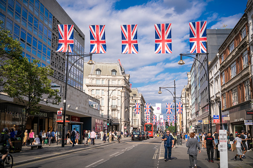 London Oxford Street with Red Bus and London taxi and people walking on street. Is a Westminster commercial street with more than 300 shops, crossing Oxford Circus. Starting in Marble arch to Hyde Park. With UK flags crossing the street and also LGTBIQ+ flags