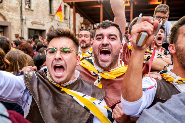 The emotion and exultation of some supporters during the Palio competitions in a medieval town in Umbria Gualdo Tadino, Umbria, Italy, October 02 -- A scene from the traditional Palio di San Michele Arcangelo (Palio of St Archangel Michael) in the medieval town of Gualdo Tadino, in Umbria. An ancient three-day festival that involves the entire community in a traditional Corteo Storico (Historical and Allegoric Parade) and culminates with a donkey race between the four 'contrada' (districts) of this medieval town. In the photo, the emotion and exultation of some supporters in medieval costume during the Palio races. An important center since Roman times, Gualdo Tadino rises between Foligno and Gubbio along the ancient Flaminia consular road, traced by the Romans. Its history spans the entire Middle Ages and, despite being partially destroyed and sacked several times and placed under the dominion of Perugia, this ancient Umbrian center still retains its medieval charm. The Umbria region, considered the green lung of Italy for its wooded mountains, is characterized by a perfect integration between nature and the presence of man, in a context of environmental sustainability and healthy life. In addition to its immense artistic and historical heritage, Umbria is famous for its food and wine production and for the high quality of the olive oil produced in these lands. Image in high definition format. gualdo tadino stock pictures, royalty-free photos & images