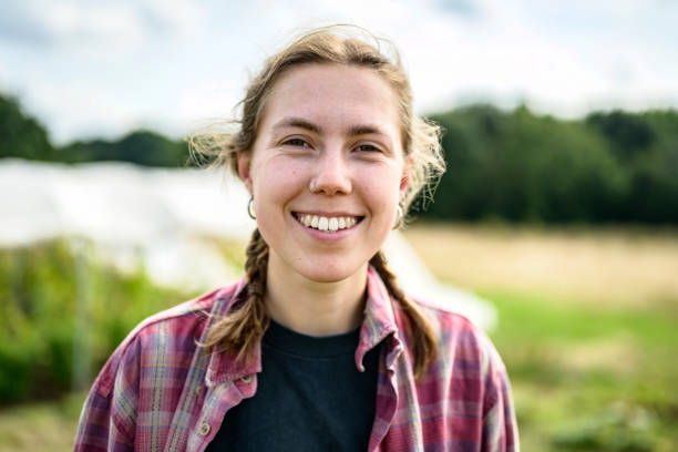 Informal outdoor portrait of cheerful young farmworker Head and shoulders view of Caucasian woman with braided hair wearing plaid shirt over t-shirt and smiling at camera. english farmer stock pictures, royalty-free photos & images