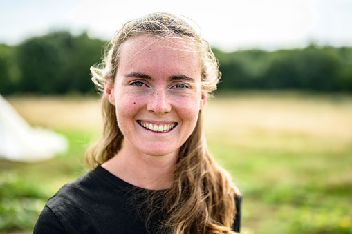 Headshot of Caucasian woman with long windblown hair standing outdoors on smallholding farm and smiling at camera.