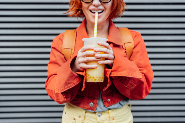 istock Fruity sugar flavored tapioca pearl bubble tea with straw is drinking by smiling hipster fashion young woman in bright clothes on the gray striped wall background. Selective focus. Copy space 1432274126