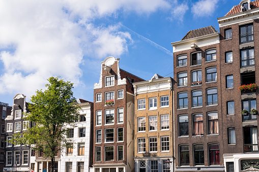 Side view of a series of different townhouses and apartment buildings along the side of a canal in the historic centre of Amsterdam.