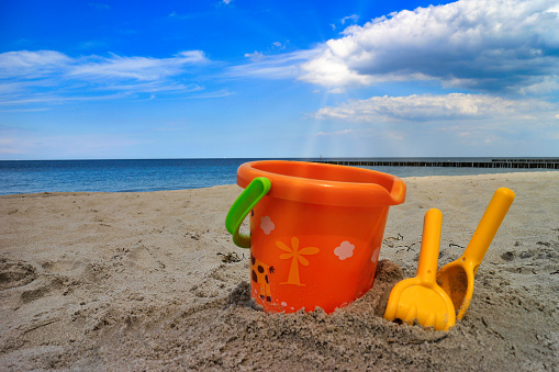 Toy bucket with shovel and fork in the sand of a beach at summertime
