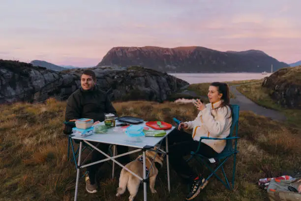 Photo of Woman and man admiring the pink  sunset having picnic by the sea with mountain view in Norway