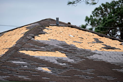 Wind damaged house roof with missing asphalt shingles after hurricane Ian in Florida. Repair of home rooftop concept.
