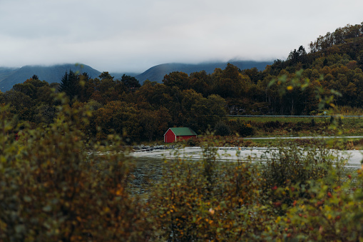 Scenic view of the red boat house at the sand beach with view of the fall woodland and the mountain peaks in More og Romsdal county, Norway