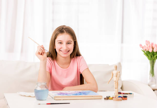 Beatiful teen girl drawing from wooden action figure with watercolor paint