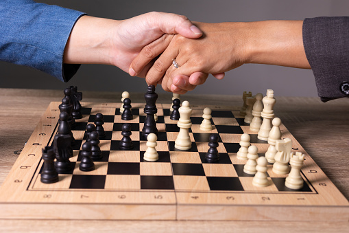 Close up 4K of two business mans playing chess and shakehand after winning the game. It shows concept of competition with strategic business planning and doing business deal with partnership.