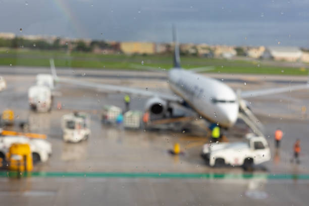 Blurred background and window view with rain drops of airplane which is ready for departing on runway and seeing passengers and luggage for travelling shows concept of airline transportation.
