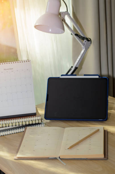 istock Desk for student concept. Tablet for study for exam, book place on School table for student work online at home. Desktop Calendar, notebook, book, and Lamp place on wooden desk-vertical Image. 1432287066